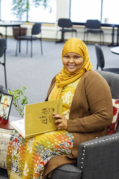 ESL LINC Student Reading a Book and Smiling in Brooks Campus Library