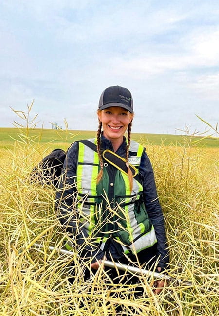 Tahnee Darmanin sits in a field of tall yellow grass with safety vest and hat on