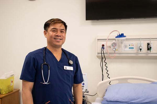 Health Care Aide Alumni Student, Jerry Tengco, standing in the medical simulation lab.