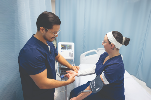 A Health Care Aide student taking another student's blood pressure