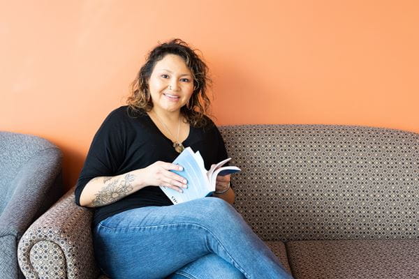 Student reading a book on a patterned couch with an orange wall behind