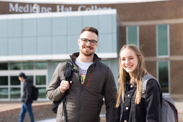 Two students stand outside MH campus main entrance