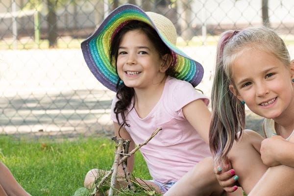 Two girls sitting in the grass playing with sticks and leaves