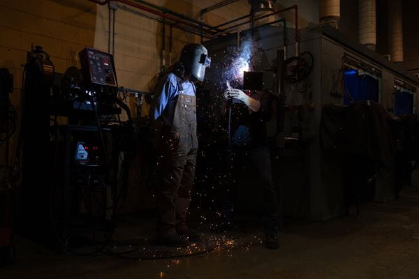 Person with welding mask watching another person weld with welding mask. 