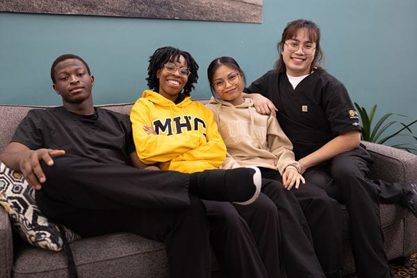 Group of students sitting on a couch, smiling at the camera. 