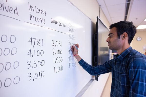 Student writing accounting numbers on a whiteboard