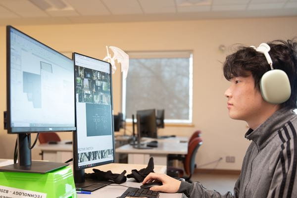 Student working on the computer with two monitors and headphones on