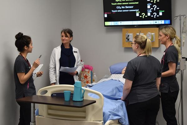 Nursing students and instructor standing around hospital bed 