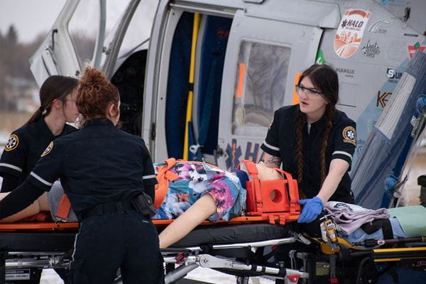 Paramedic students loading simulation mannequin on stretcher into ambulance
