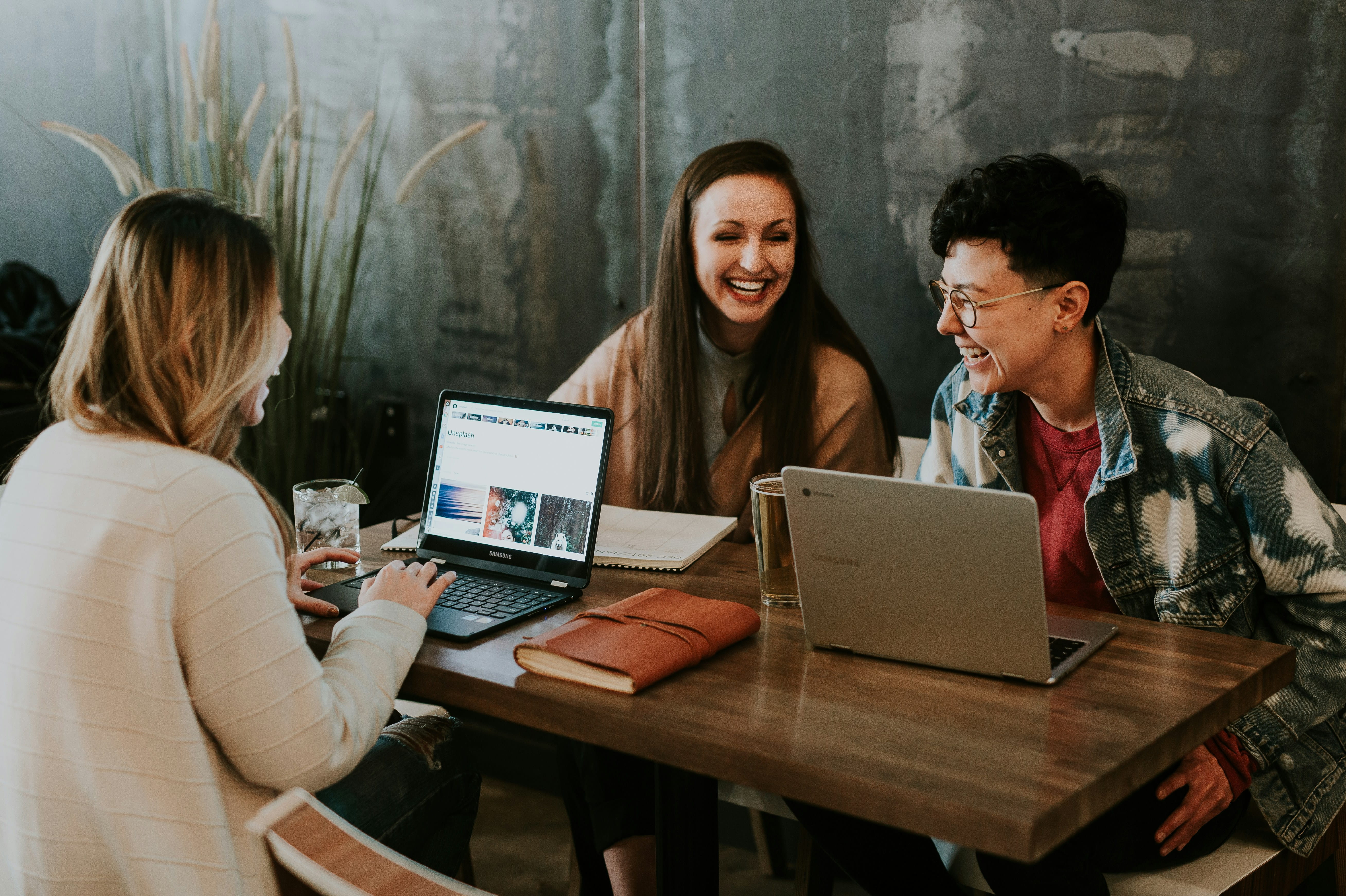 Three people laughing while working on laptops at a table. 