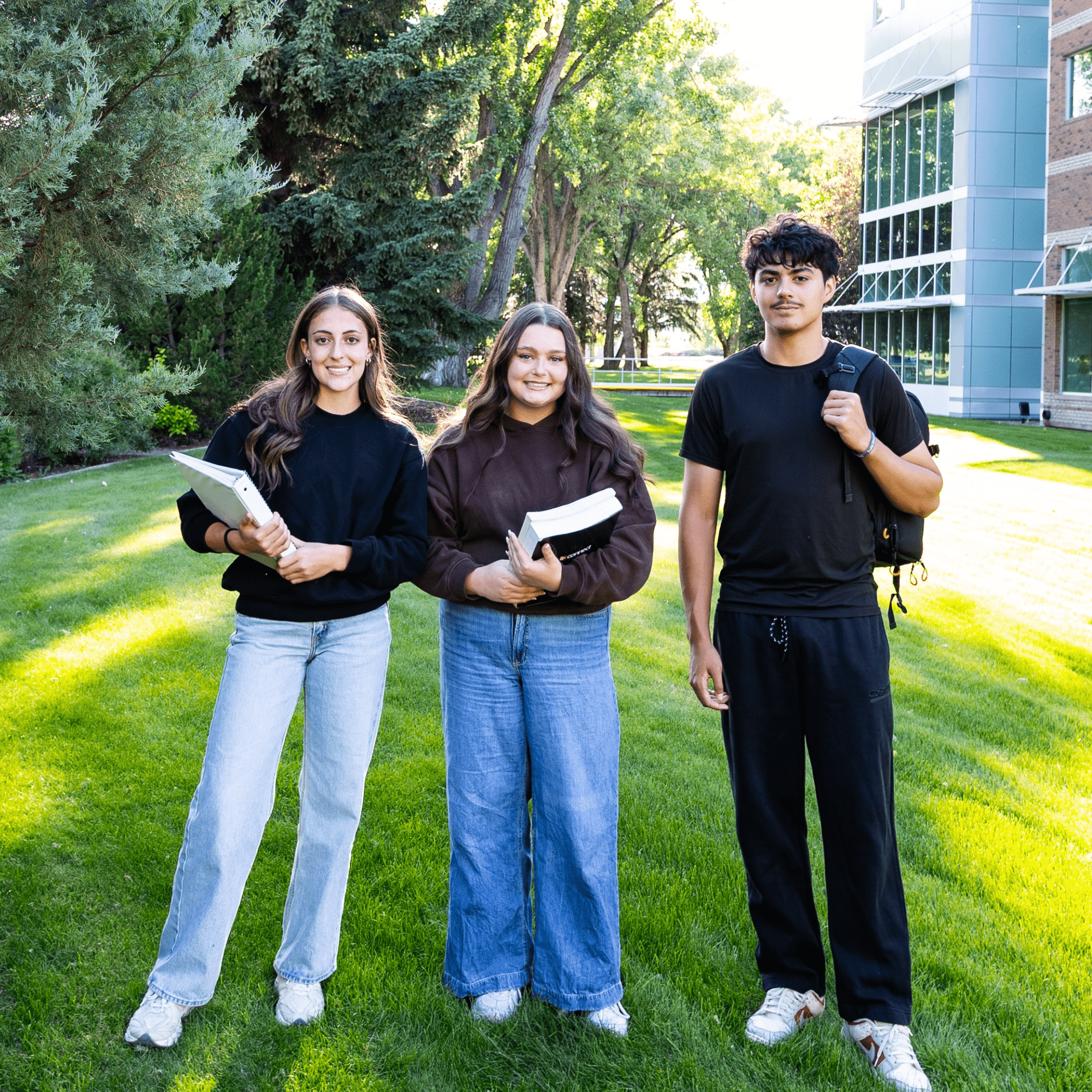 Three students holding textbooks and backpacks standing together outside at Medicine Hat College