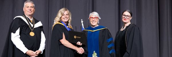 Close up of Nichole Neubauer accepting award with Executive members at convocation.