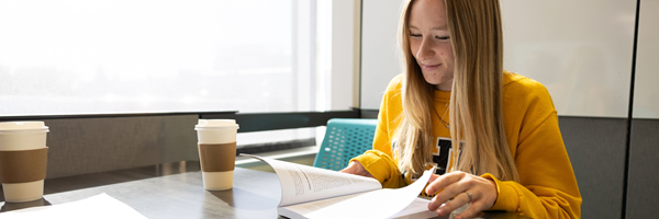 Student studying at table with book and coffee.