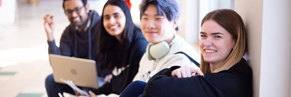 Four students smiling, sitting on hallway bench