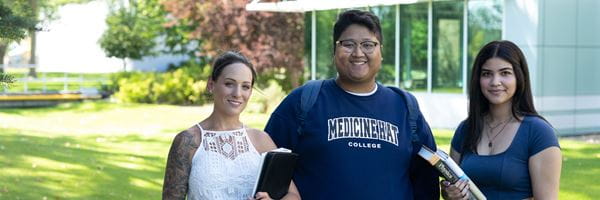 Three students standing outside Medicine Hat campus during summer