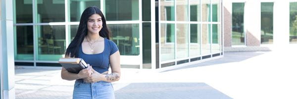 Student holding textbooks standing outside of MHC