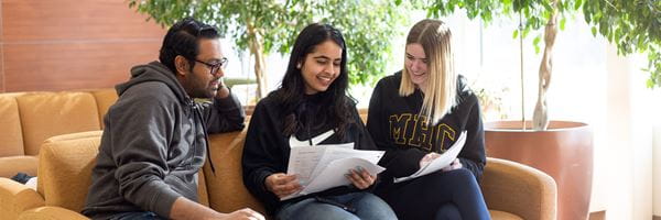 Three students sitting on a couch looking at study notes