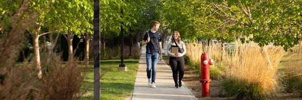 Two students walking on a sidewalk.