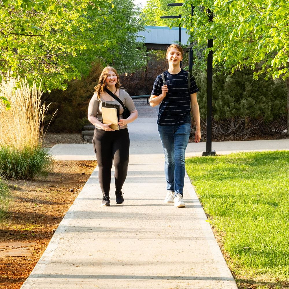 Two students holding books and walking on a path