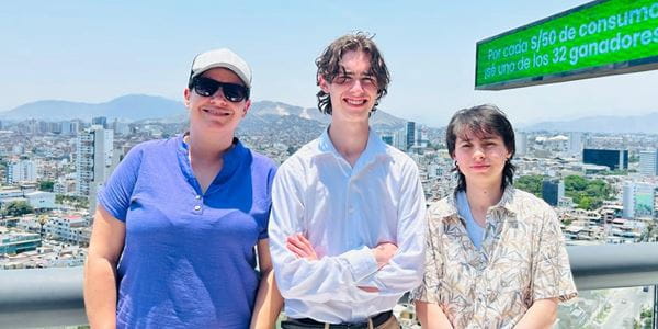 Study Abroad students standing outside with buildings and mountain in the background. Tara Holland, Barrett Long, and Janine Zuniga.