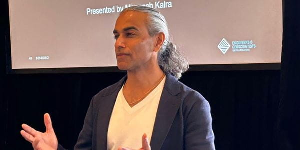 Maneesh Kalra in front of screen, speaking to audience. 