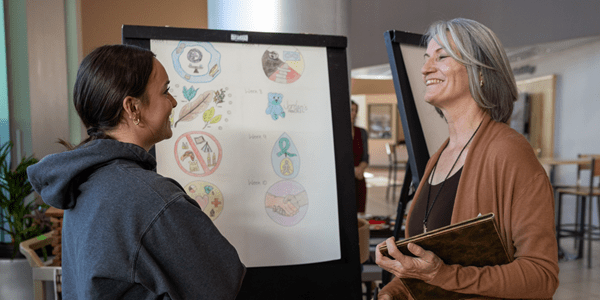 Nursing student and instructor smiling in front of student artwork.