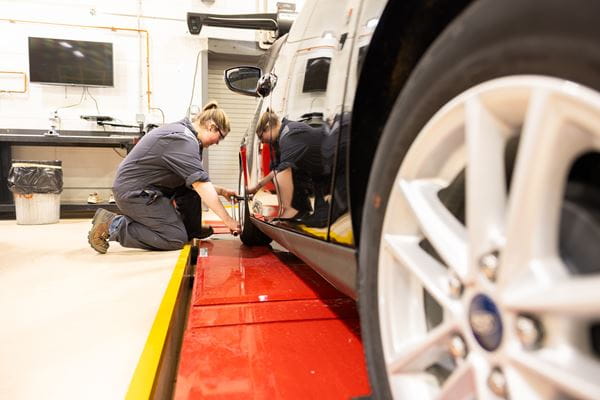 A female apprentice is changing a tire on a car in the Medicine Hat College Automotive Service Technician lab 
