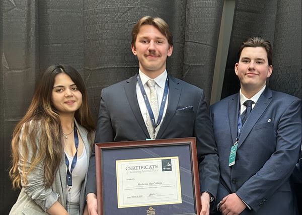 Close up of three business students in suits, holding a framed certificate. 