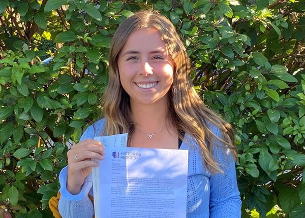 Close up of Abigail Pohl holding up a cheque and letter in front of green shrub.