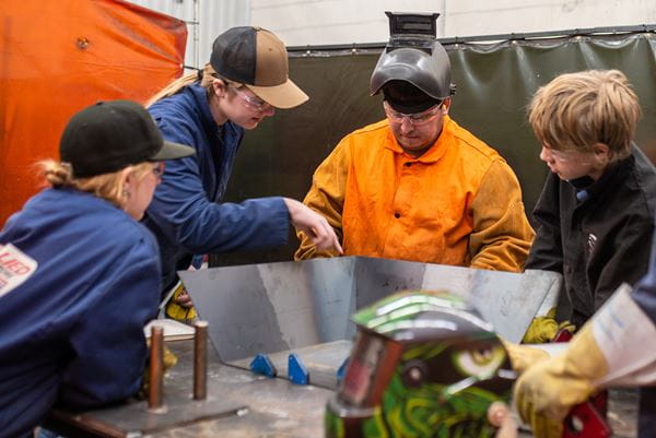 Three students experience trades education in a welding lab