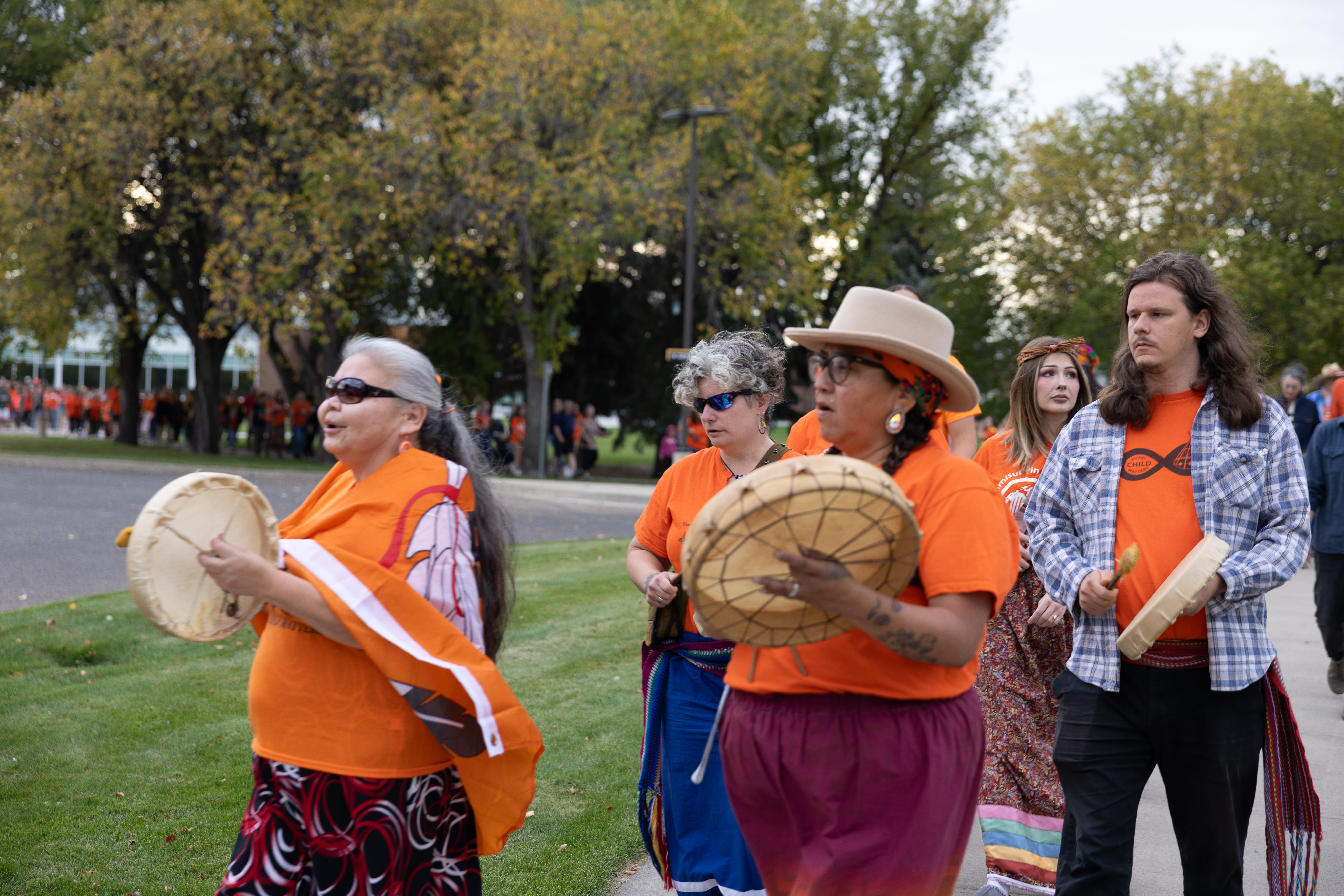 Indigenous drummers lead a walk for reconciliation where several community members are following and wearing orange shirts.