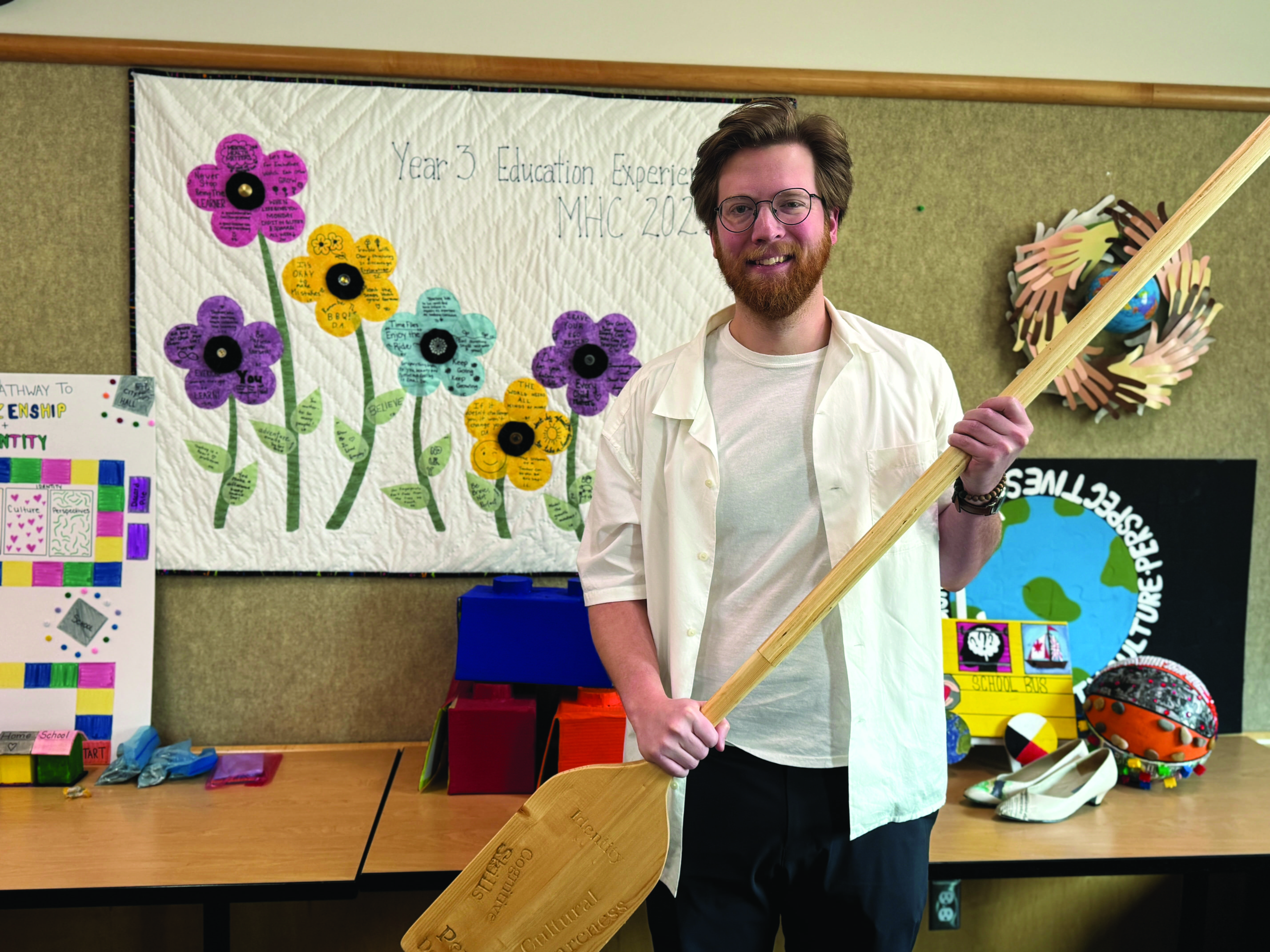 A male student with brown hair and facial hair holds a canoe he crafted for a project in the Bachelor of Education program
