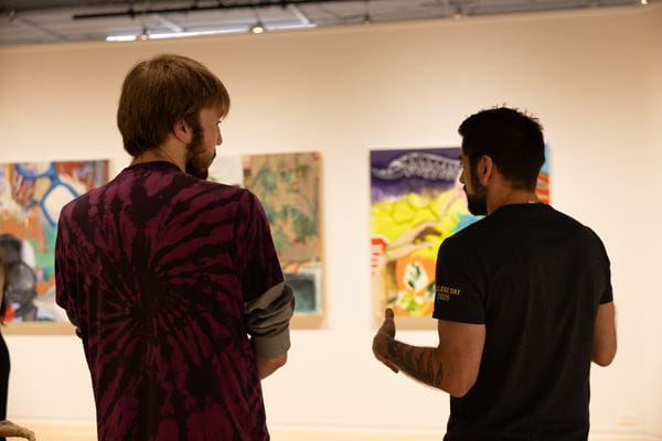 Two men look at several art pieces.