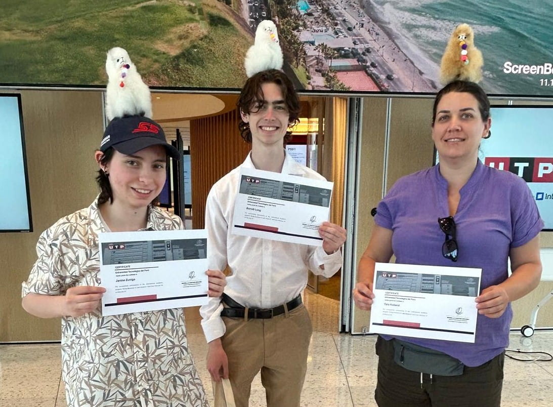 Study Abroad students standing with certificate and a stuffed animal on top of the students head. Janine Zuniga, Barrett Long, and Tara Holland.