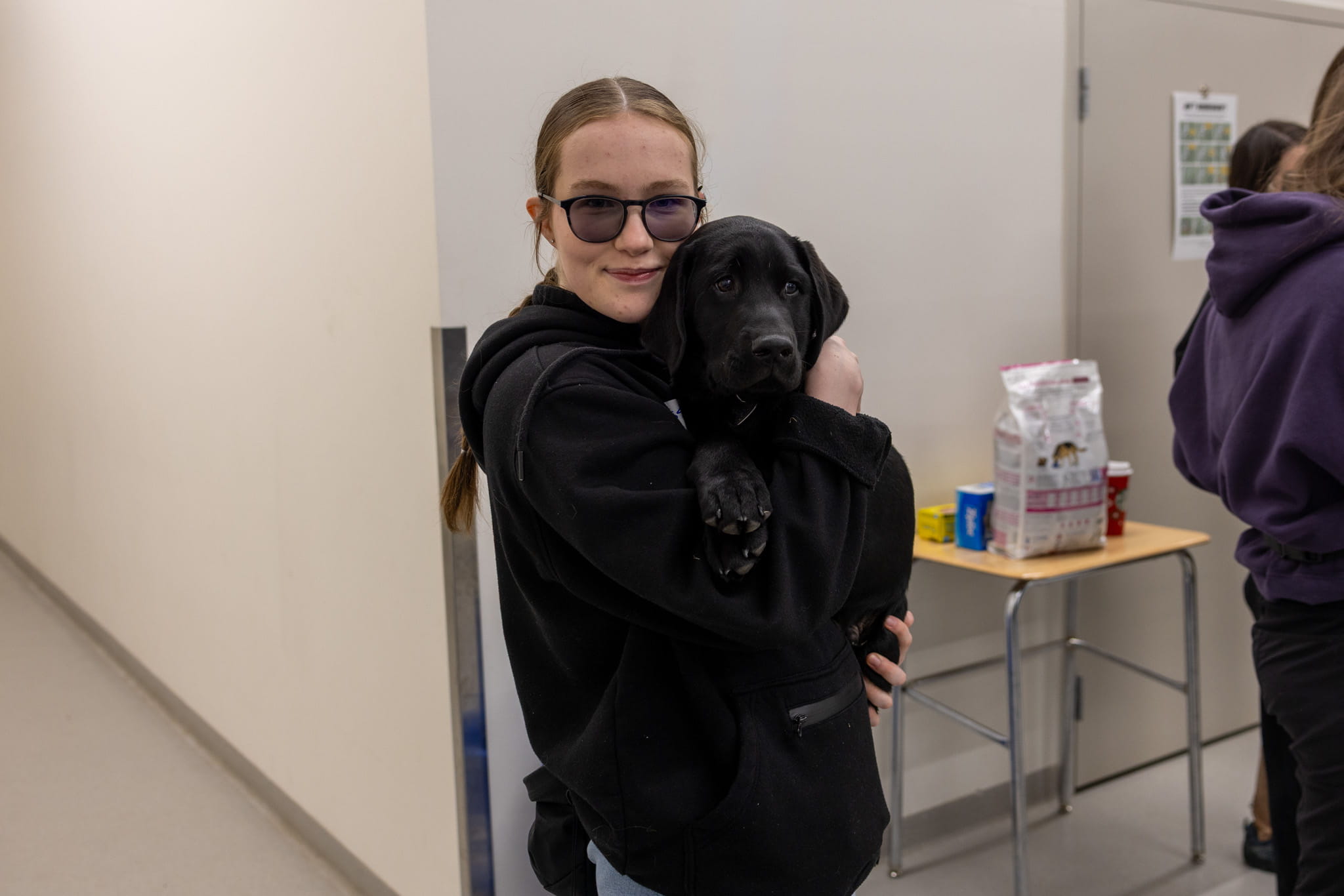 Service Dog & Canine Studies Management Diploma student, Sarah Shields hugs puppy to herself and smiles at camera.