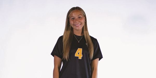 A female student wearing a Rattlers jersey with the number 4 smiles at the camera.