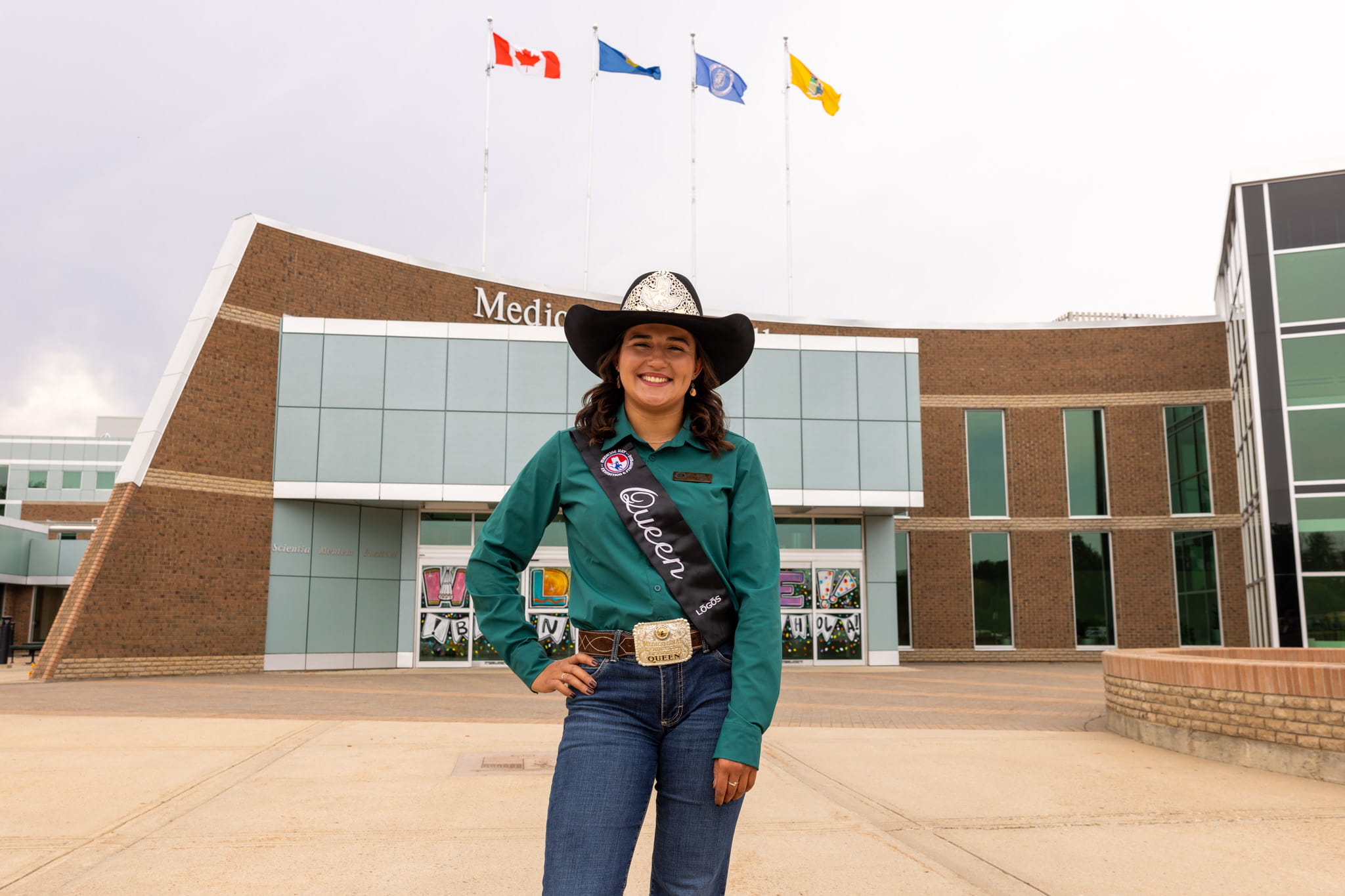 Woman in cowboy hat in green shirt stands outside of brick building.