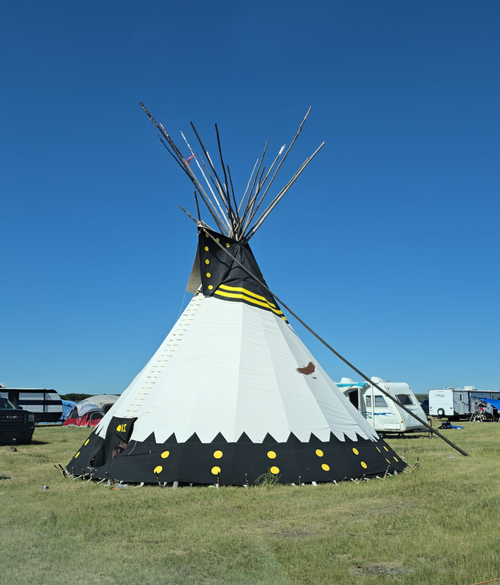Medicine Hat College Tipi set up on green grass and a blue clear sky in the background.