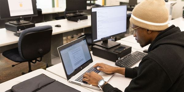 Student in library working on laptop and on a computer. 