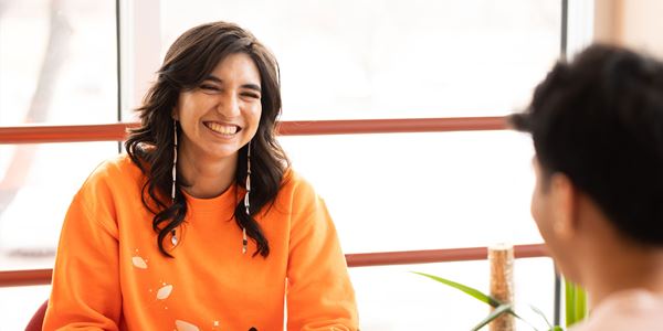 Student in orange sweater smiling at a friend