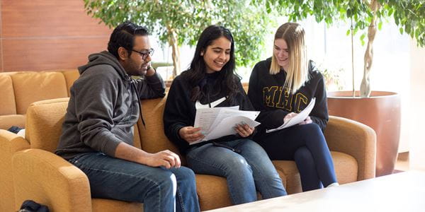 Three students sitting on a couch studying 