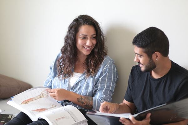 Students study textbooks together while sitting on bed in residence room