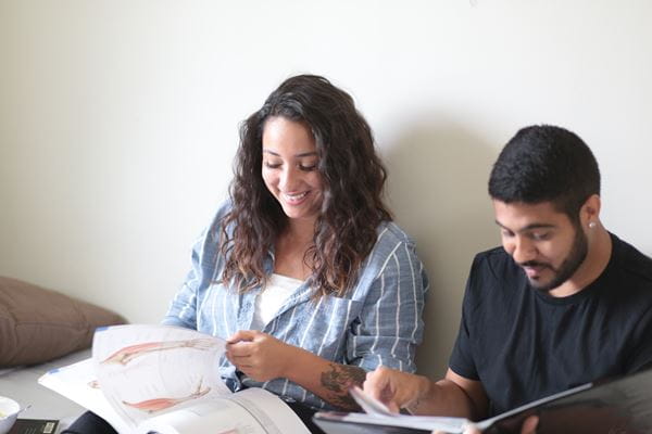 Students study textbooks together while sitting on bed in residence room