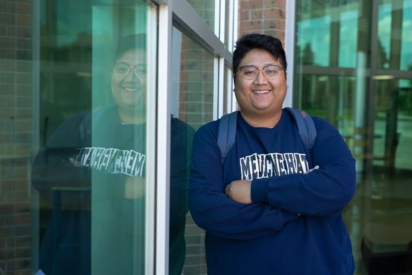 Student leaning up against outside window of Centennial Hall with mirror reflection